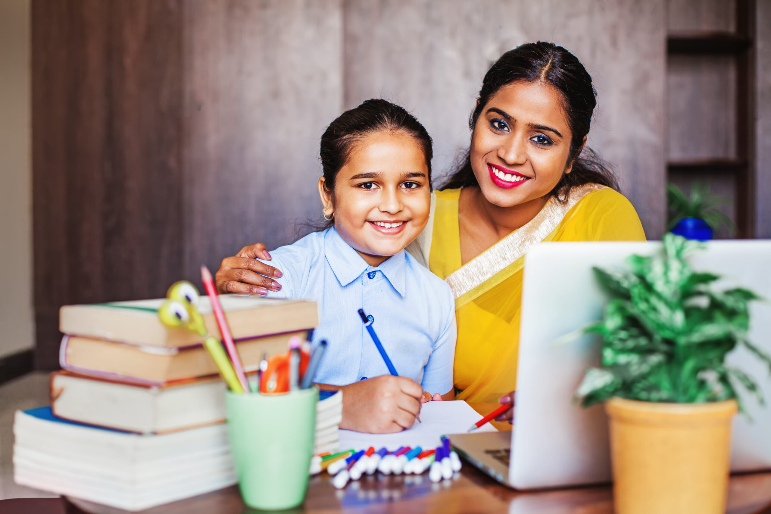 Indian mother and her daughter posing while doing homework with the help of laptop
